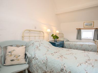 A bedroom with two single beds a blue bedside table with lamps a chair with a cushion and a small window at Bryn Eira Stables in Llanfair PG