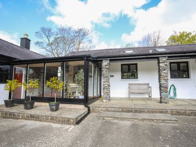 An outdoor patio area with potted plants bench and a glass enclosed seating area at Bryn Eira Stables in Llanfair PG
