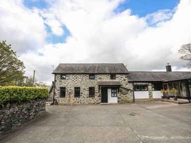 A stone cottage with black framed windows and a concrete driveway at Bryn Eira Stables in Llanfair PG