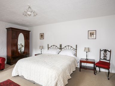 A bedroom with a double bed table lamps a wooden wardrobe a red chair and two framed pictures at Bryn Eira Stables in Llanfair PG