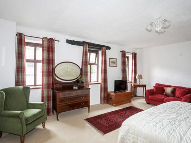 A bedroom with a bed red sofa green armchair wooden chest and dresser with mirror at Bryn Eira Stables in Llanfair PG