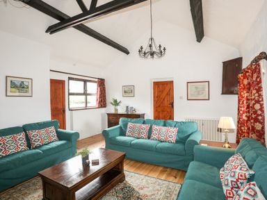 A living room with teal sofas and patterned cushions a wooden coffee table and beams on the white ceiling at Bryn Eira Stables in Llanfair PG