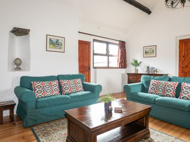 A living room with two green sofas with patterned cushions a wooden coffee table and a side cabinet at Bryn Eira Stables Llanfair PG