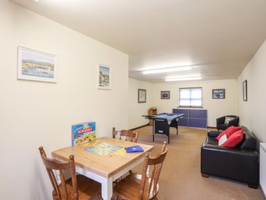 A game room with a wooden table and chairs with a scrabble game a pool table a black leather sofa with red pillows and framed pictures on the walls at Bryn Eira Stables in Llanfair PG