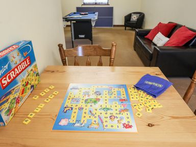 A game room with a junior scrabble board on a wooden table and a pool table sofa and chair in the background at Bryn Eira Stables Llanfair PG