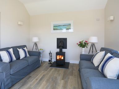 A living room with two blue sofas white cushions a wood burning stove and two lamps at Bwthyn Glanrhyd in Llanfair yn Neubwll
