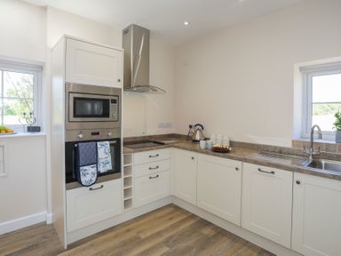 A kitchen with white cabinets a built-in oven and microwave countertop appliances and a window at Bwthyn Glanrhyd in Llanfair yn Neubwll