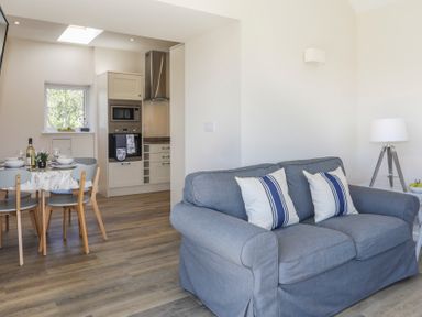 A living room with a gray sofa and two pillows next to a dining table and kitchen at Bwthyn Glanrhyd in Llanfair yn Neubwll