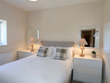 A bedroom with a bed and two bedside tables with lamps and mirrors at Bwthyn Glanrhyd in Llanfair yn Neubwll