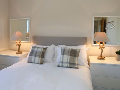 A bedroom with a bed with pillows two bedside tables with lamps and mirrors at Bwthyn Glanrhyd in Llanfair yn Neubwll
