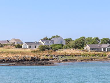 Houses near a rocky shore with water in the foreground and trees in the background at Bwthyn Glanrhyd in Llanfair yn Neubwll