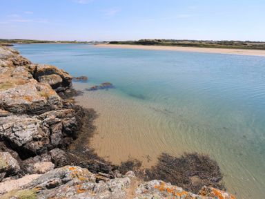 A coastal scene with rocks and clear water next to a sandy beach at Bwthyn Glanrhyd in Llanfair yn Neubwll