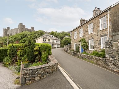 A street with stone houses and a castle on a hill in the background at Bron Castell in Harlech