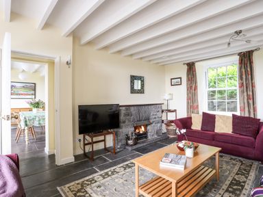 A living room with a maroon sofa a wooden coffee table a television a stone fireplace and a window with curtains at Bron Castell in Harlech