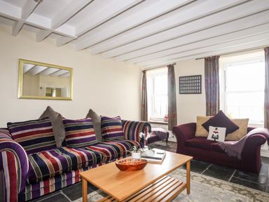 A living room with striped sofa cushions a wooden coffee table and two windows with curtains at Bron Castell in Harlech