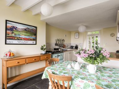 A kitchen with wooden table and chairs a floral tablecloth and flowers in a vase at Bron Castell in Harlech