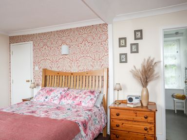 A bedroom with a wooden bed and a chest of drawers with a vase and lamp at Bron Castell in Harlech