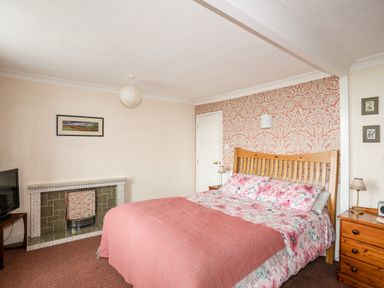 A bedroom with a double bed floral bedding a wooden headboard two bedside tables a fireplace a television and wallpaper at Bron Castell in Harlech