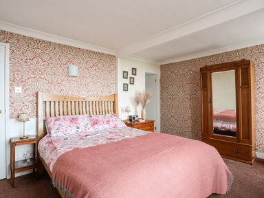 A bedroom with a wooden bed frame and floral bedding with a pink blanket at Bron Castell in Harlech