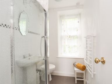 A bathroom with a shower enclosure a sink a toilet a small stool with a towel and a window at Bron Castell in Harlech