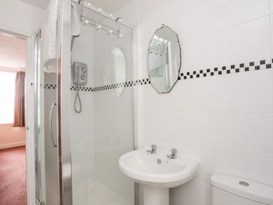 A bathroom with a glass shower enclosure a wall-mounted shower unit a white sink with two taps a mirror above the sink and a toilet at Bron Castell in Harlech