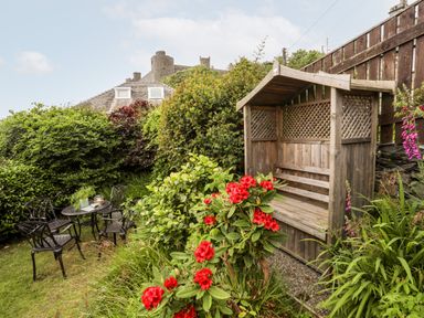 A garden with a wooden bench shelter red flowers and black metal table and chairs at Bron Castell in Harlech
