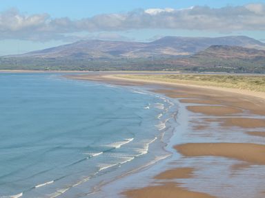 A sandy beach with waves and hills in the background at Bron Castell in Harlech
