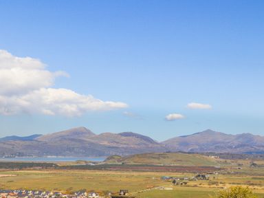 A rural landscape with houses fields hills and mountains under a blue sky at Bron Castell in Harlech