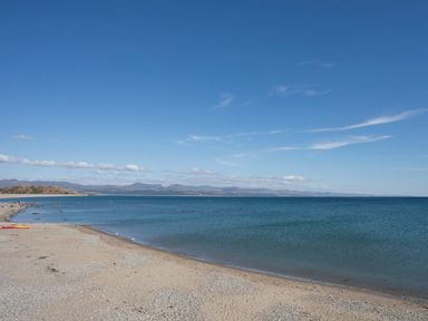 A sandy beach with small pebbles next to a calm sea under a clear blue sky with distant mountains at Brook Cottage in Criccieth