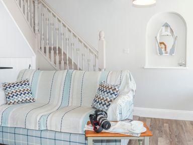 A living room with a striped throw on a sofa and a camera on a wooden table at Brook Cottage in Criccieth