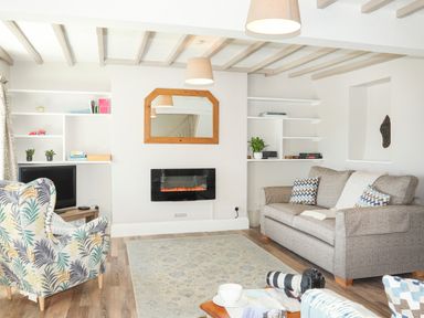 A living room with a sofa an armchair a wall-mounted electric fireplace and shelves at Brook Cottage in Criccieth