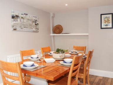 A dining room with a wooden table set for six and wall art at Brook Cottage in Criccieth