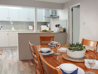 A dining table set with plates glasses and a plant with a kitchen area in the background at Brook Cottage in Criccieth