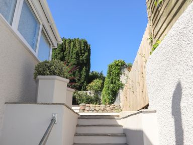 Outdoor stairs with plants on the stone wall and a wooden fence under a clear sky at Brook Cottage in Criccieth