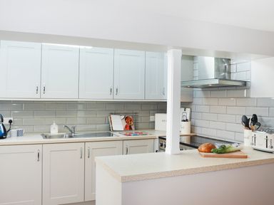 A kitchen with white cabinets a countertop with bread vegetables and kitchen appliances at Brook Cottage in Criccieth