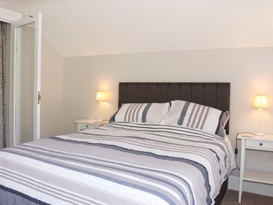A bedroom with a double bed striped bedding two bedside tables with lamps at Brook Cottage in Criccieth