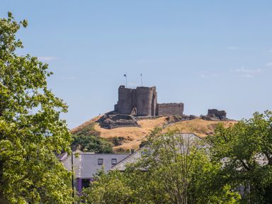 A ruined stone castle on a hill behind buildings and trees at Brook Cottage in Criccieth