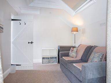 A small living room with a gray sofa a floor lamp a white storage unit and a white door at Brook Cottage in Criccieth