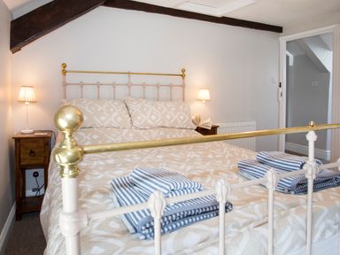 A bedroom with a bed with patterned bedding and striped towels on it with bedside tables and lamps at Brook Cottage in Criccieth