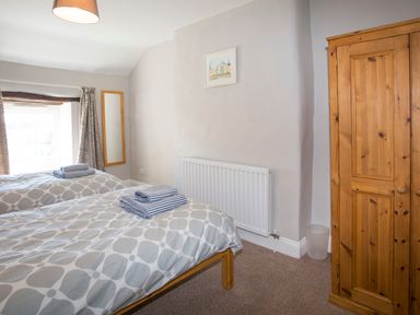 A bedroom with two single beds with folded towels on each bed a wooden wardrobe a wall mirror and a window at Brook Cottage in Criccieth