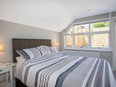A bedroom with a bed with striped bedding and two bedside tables with lamps at Brook Cottage in Criccieth