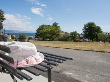 A white hat with pink flowers on a black bench overlooking a park with trees and houses in the background at Brook Cottage Criccieth