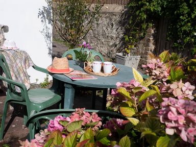 A green plastic outdoor table and chairs with two mugs on a tray a hat and flowers at Bro Dawel in Beaumaris