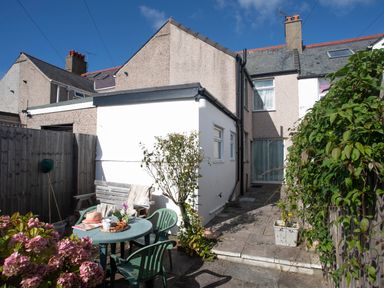 A small patio with a round table and chairs outside a house with a white extension at Bro Dawel in Beaumaris