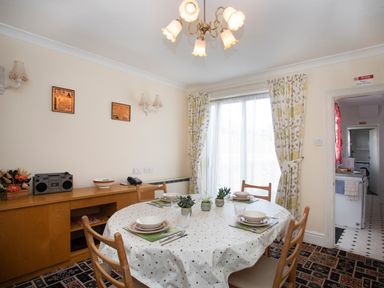 A dining room with a round table set for four and floral curtains at Bro Dawel in Beaumaris