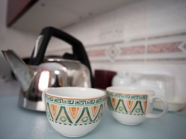 Two decorated cups on a kitchen counter next to a metal kettle at Bro Dawel in Beaumaris