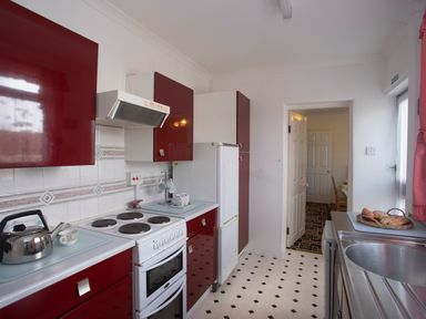 A kitchen with red cabinets a white stove a refrigerator and a sink at Bro Dawel in Beaumaris