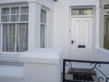 A white front door with Bro Dawel written above and a nearby window with white curtains at Bro Dawel in Beaumaris