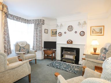 A living room with armchairs a fireplace and a television at Bro Dawel in Beaumaris