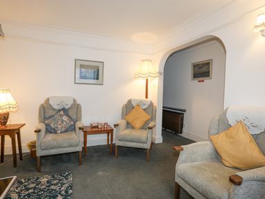 A sitting room with armchairs, side tables, lamps and framed pictures at Bro Dawel in Beaumaris